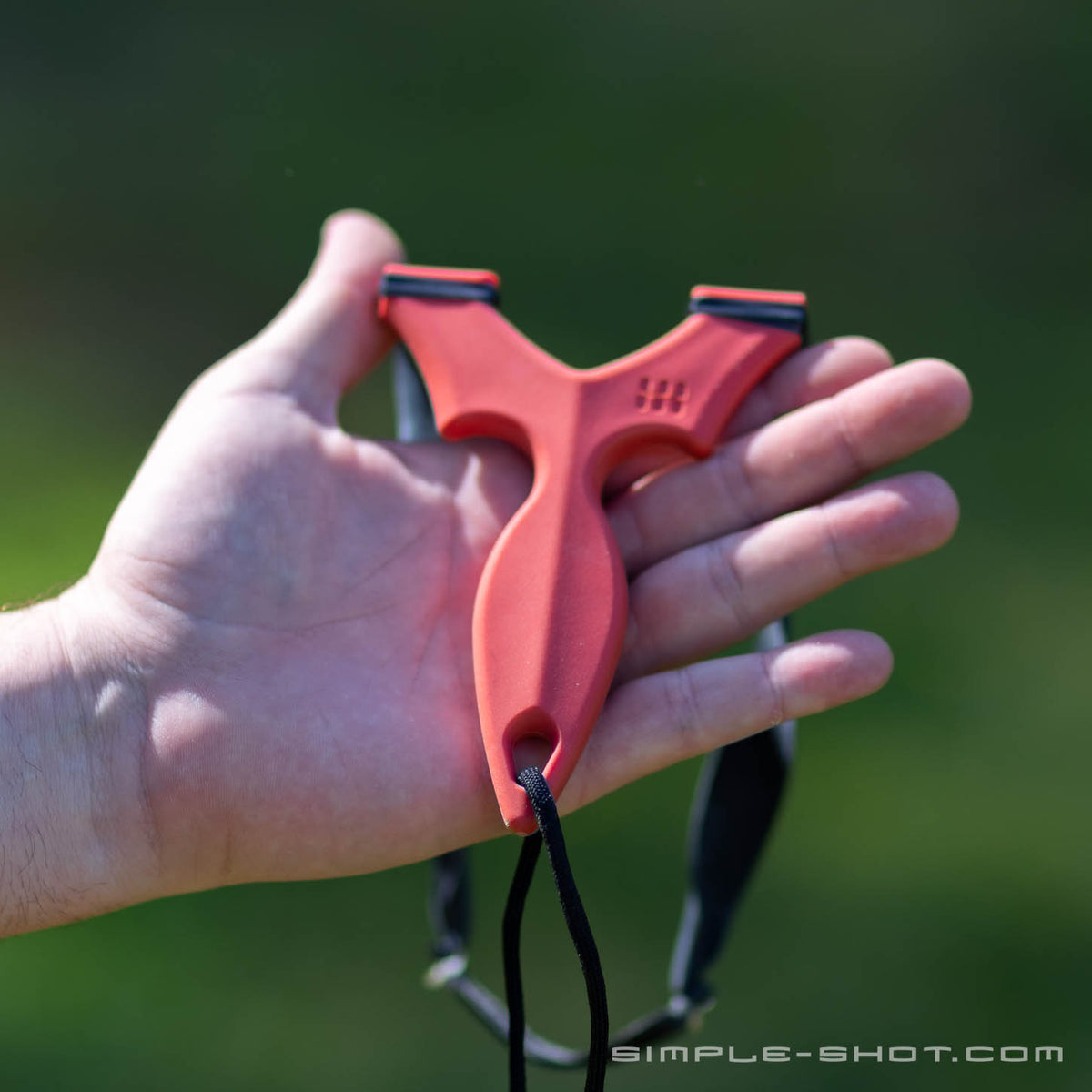 Red Stylus Revolve slingshot resting in an open palm outdoors