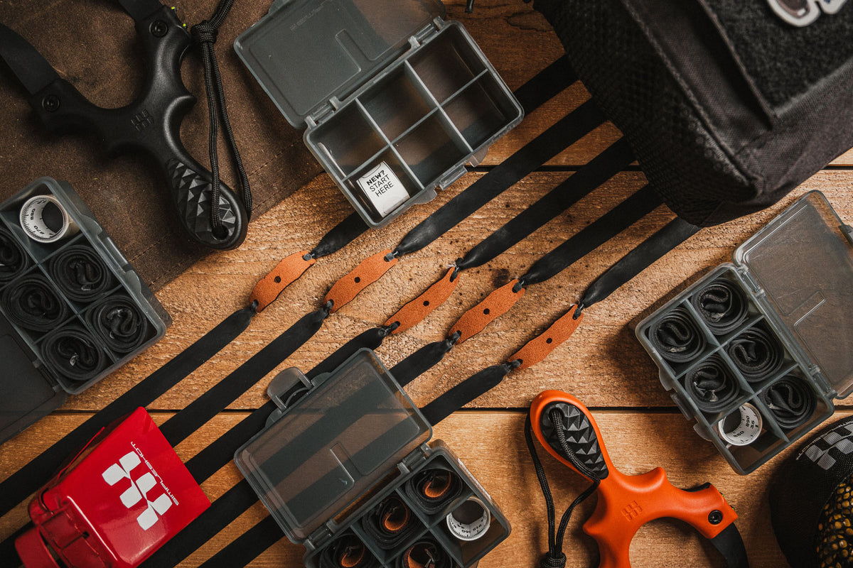 Clay shooting bandsets laid out with slingshots and gear on a wood bench