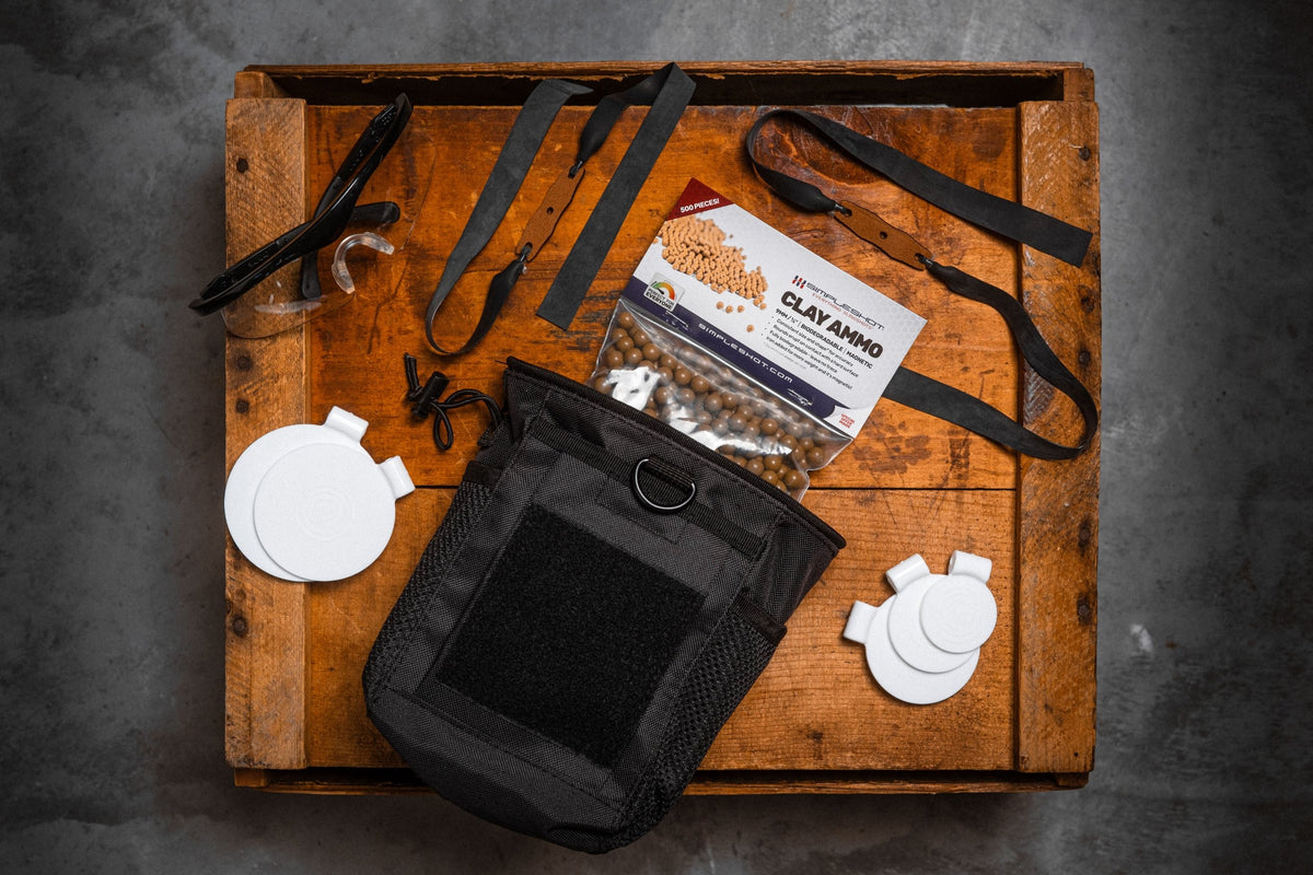 Clay ammo, two clay bandsets, five spinner targets, a carry bag, and safety glasses laid out on a wooden crate