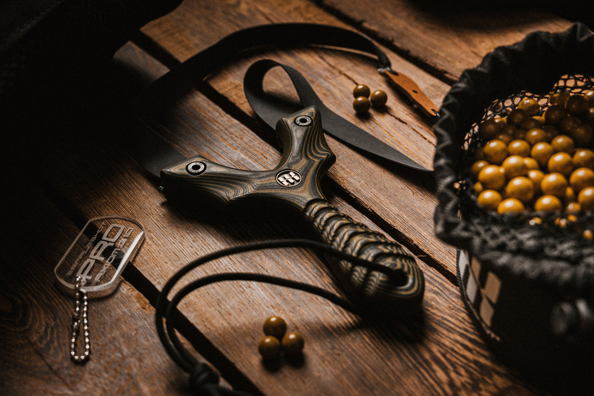 Axiom PRO G10 slingshot with clay ammo and gear on wood
