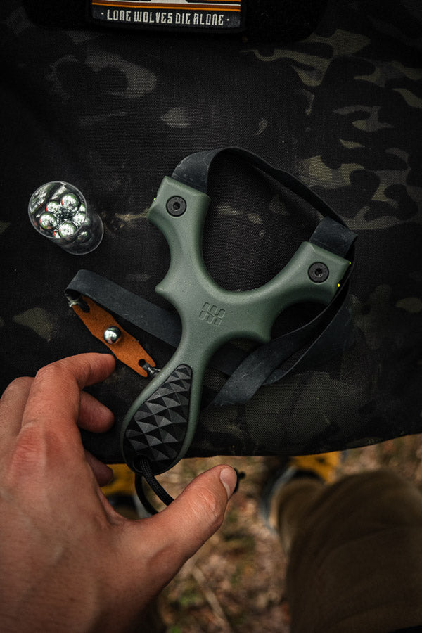 A hand reaching for a green Scout LT2 slingshot on a pack