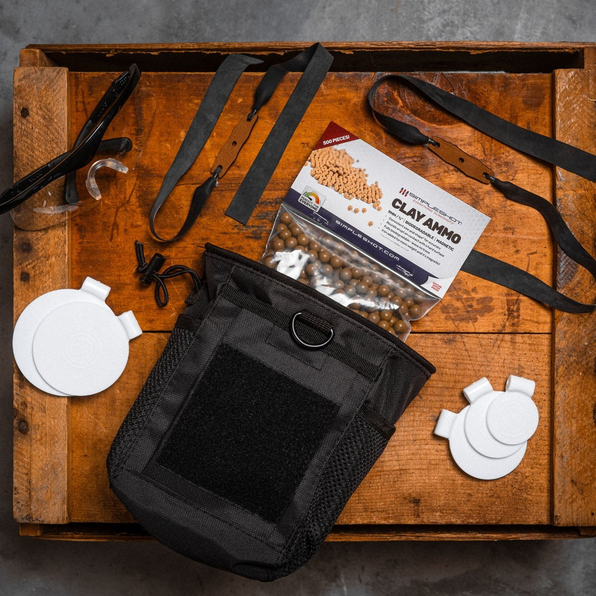 Clay ammo, two clay bandsets, five spinner targets, a carry bag, and safety glasses laid out on a wooden crate