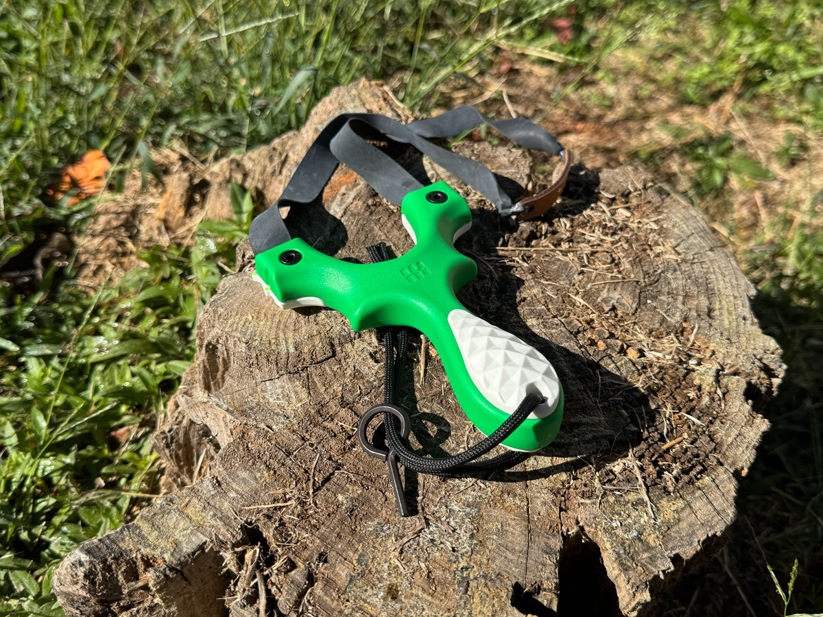Scout LT2 4-H Edition slingshot in bright green with white scales resting on a stump outdoors