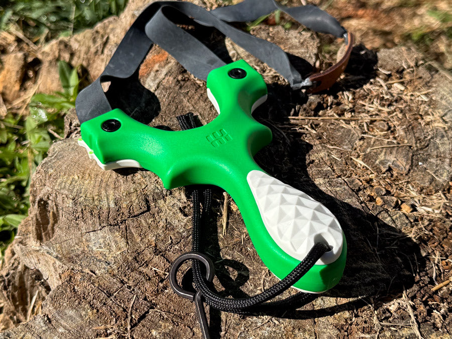 Scout LT2 Magnolia Edition slingshot in bright green with white scales resting on a stump outdoors
